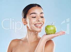 Beautiful young mixed race woman with an apple isolated in studio against a blue background. Her skincare regime keeps her fresh. For glowing skin, eat healthy. Packed with vitamins and nutrients