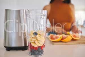All you need is a smoothie. a woman putting a variety of fruits into a blender at home.