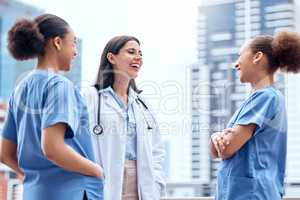 Young caucasian doctor in a lab coat standing outside and talking to mixed race nurses in scrubs. Diverse group of healthcare professionals. African American medical nurses in uniform with a physician