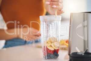 Smooth up your day. a woman putting a variety of fruits into a blender at home.