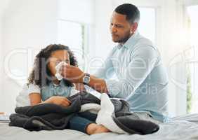 A fathers love will nurture you back to health. Shot of a young father blowing his sick daughters nose at home.