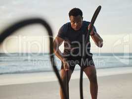 Man doing workout using two battle ropes on the beach. Fit african american man exercising by the sea. Dedicated to fitness