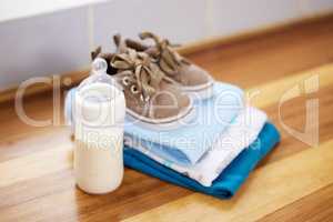 The new baby starter pack. baby clothes and a milk bottle on a table at home.