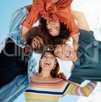 Cheerful group of diverse friends standing in a huddle against a blue sky. Multi-racial millennial friends standing together arms around each other and smiling while looking down at the camera