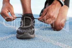 Active athletic man preparing for a practice run to increase stamina for a competitive race on an Olympic track. Closeup of a fit african american athlete tying his shoelaces before running outside.