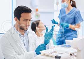 Deep in through during the selection process. Shot of a dentist applying his gloves while selecting the tool he needs.