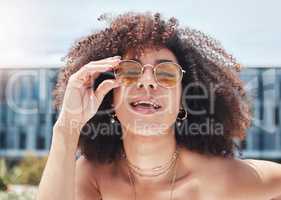 Young mixed race woman with curly natural afro hair wearing trendy and stylish sunglasses outside. One female only looking carefree, cool and confident. Happy fashionable hispanic woman in the city