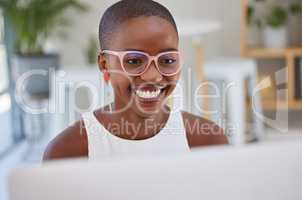 Young african american businesswoman wearing glasses, smiling and working on a computer in an office. One female only browsing online while planning on a desktop pc at her desk. Confident hard working black female entrepreneur completing deadlines and sen