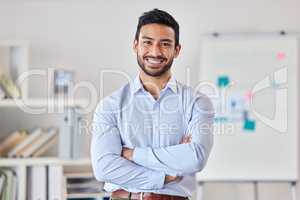 Young happy mixed race businessman standing with his arms crossed working alone in an office at work. One expert proud hispanic male boss smiling while standing in an office