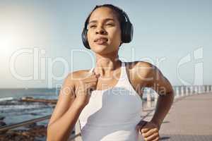 Close up of fit young female athlete in sportswear wearing wireless headphones and listening to music while out for a run along the promenade. Exercise is good for you health and wellbeing