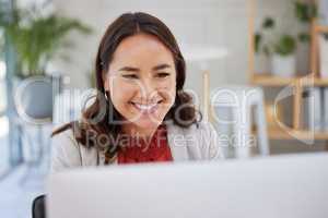 Young smiling asian businesswoman sitting alone in an office and browsing the internet on a computer. Ambitious creative professional networking and emailing clients at a desk. Entrepreneur at work