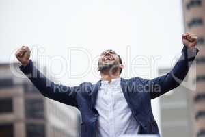 The sweet release. a handsome young businessman standing outside in the city with his arms raised in jubilation.