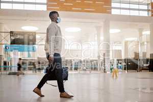 African american businessman travelling alone and walking in a train station while wearing a mask for protection against coronavirus. Young black male on his way to work in a station in the morning
