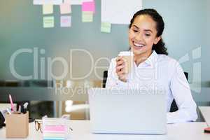 Coffee puts me in a good mood. an attractive young businesswoman sitting alone in the office and enjoying a coffee while using her laptop.
