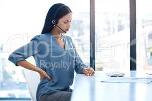 Her job has become a lot more stressful. Shot of a young call centre agent experiencing back pain while working in an office.