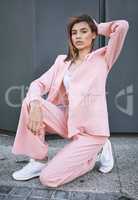 Portrait of a young trendy and confident mixed race woman looking stylish while posing and spending time in the city. Fashionable hispanic female model wearing pink clothes and kneeling on the concrete ground time in the city