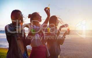 using the majesty of nature. a group of female friends using the breeze to blow bubbles.