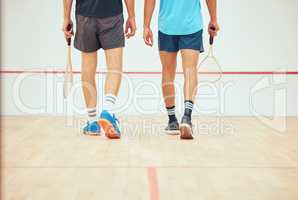 Rear view of two unknown squash players walking together on court and holding rackets before game. Fit active mixed race and caucasian athlete getting ready for training and practice in sports centre