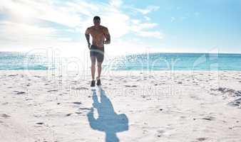 Fit young black man running and jogging on sand at the beach in the morning while exercising. One strong male bodybuilder athlete with six pack abs doing cardio workout to build muscle and endurance