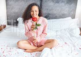 I wonder who left me this.... Full length shot of an attractive young woman smelling a rose while sitting cross-legged in her bedroom at home.