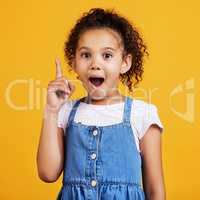 Studio portrait mixed race girl pointing upwards towards copyspace isolated against a yellow background. Cute hispanic child posing inside. Happy and cute kid showing or endorsing a company or product