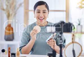 Happy young beauty blogger holding up a beauty product and sponge while doing a make-up tutorial and recording with her tripod. Influencer working as a brand ambassador for beauty products on social media