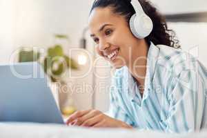 Time for rest and relaxation. Shot of a young woman listening to music while using a laptop on her bed at home.