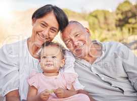 Happy mixed race grandparents sitting with granddaughter on a beach. Adorable, happy, hispanic baby girl bonding with grandmother and grandfather in a garden or park outside. Baby with foster parents