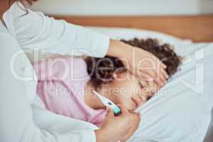 Sick mixed race girl lying asleep in bed at home. Worried mother using thermometer and her hand to feel the high body temperature on her little daughters forehead for symptoms of fever, flu or covid