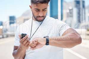 Young mixed race male athlete checking digital chronometer and smart watch to track time during a workout. Sportsman monitoring his performance or progress during a run in the city