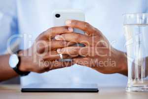 Black businessman using cellphone at his desk in an office. Hands holding phone to text and browse online