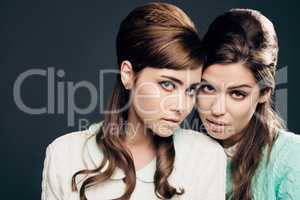 She is me and I am her. Studio shot of two attractive young women dressed up in 60s wear against a dark background.