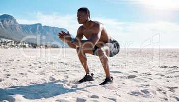 Fit young black man doing squat exercises on sand at the beach in the morning. One muscular male bodybuilder athlete with six pack abs doing bodyweight workout to build strong core, tone and endurance