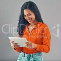 Smiling mixed race woman using digital tablet while isolated against grey studio background with copyspace. Happy young hispanic standing alone while browsing the internet and networking on technology
