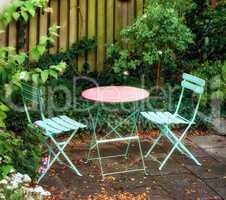 Metal chairs and table with blossoming plants in a park or private courtyard outdoors. Tranquil lush green landscape and relaxing spot in a garden to enjoy cosy picnic or quiet afternoon in spring