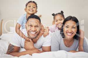 Portrait of a cheerful family lying together on bed. Little boy and girl lying on their parents laughing and having fun. Mixed race couple bonding with their son and daughter. Hispanic siblings enjoying free time with their mother and father