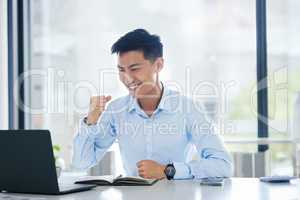 Young happy and excited asian businessman cheering with his fists working on a laptop sitting in an office alone at work. One Chinese businessperson celebrating a win. Man smiling after a success