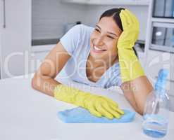 Thinking about how much shes done. a young woman smiling while cleaning a kitchen counter.