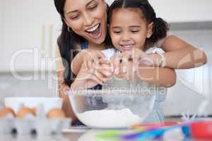 Young mother enjoying baking, bonding with her little daughter in the kitchen at home. Little latino girl smiling while helping her mother cook a meal at home. Child cracking an egg for a recipe