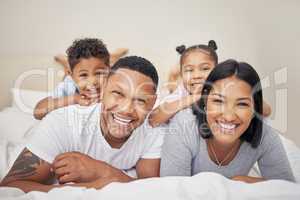 Portrait of a cheerful family with two children lying together on bed. Little boy and girl lying on their parents laughing and having fun. Hispanic siblings enjoying free time with their mother and father