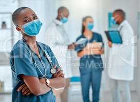 Mature african american female doctor standing with her arms crossed while working at a hospital. One expert medical professional wearing a mask while standing at work with colleagues at a clinic