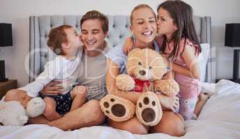 Loving children sharing tender moment with parents while gently kissing mom and dad on the cheek. Happy caucasian parents spending time with their little daughter and son at home in the morning