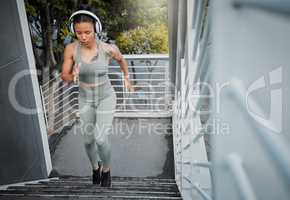 Young fit athletic mixed race woman running up stairs during outdoor workout in city while listening to music through headphones. Hispanic woman focused on health, physical activity, strength, cardio