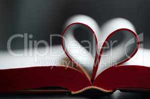 Closeup of an open book, novel with pages bent, shaped into a heart pattern to show the concept of a love to read fiction and non fiction literature. Loving reading as a hobby, pastime or way to relax
