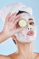 Beautiful young mixed race woman wearing a face mask peel and towel while holding cucumber slices. Attractive female clean and fresh out the shower and applying her daily skincare regime to her face