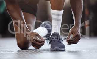 Closeup of unknown african american athlete kneeling and tying shoelaces before workout in gym. Strong, fit, active black man getting ready to exercise in health and sports centre. Preventing injury