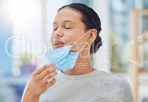 Young mixed race female patient looking relieved while removing a mask at a checkup standing at a hospital. Face of a relaxed hispanic woman wearing a mask while at a hospital
