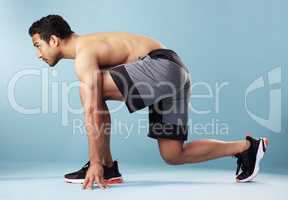 Fullbody young hispanic man standing on his mark in studio isolated against a blue background. Mixed race shirtless male runner ready to race, sprint or long distance. Endurance and cardio training