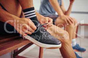 Squash player tying his shoe lace. Hands of a fit athlete getting ready for a squash match. Closeup of a player tying the laces of his sport sneaker. Player sitting on a bench with his friend.