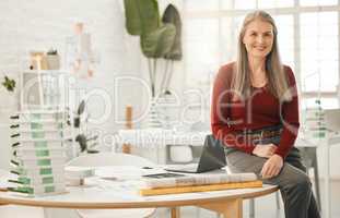 Portrait of leading businesswoman sitting on her desk. Mature businesswoman in her design agency. Creative entrepreneur working in her architecture agency. Senior corporate businesswoman in her office